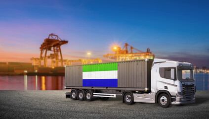 International Logistics: A modern semi-trailer truck carrying a shipping container adorned with the Sierra Leone flag stands ready for transport at a bustling port at dusk. © bao