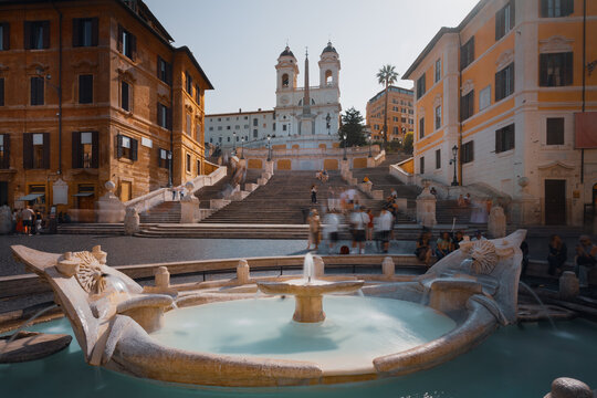 Famous Spanish Steps and Fontana della Barcaccia fountain in Rome, Italy. Beautiful landmarks of the historic city center during morning daylight with motion blurred crowd.