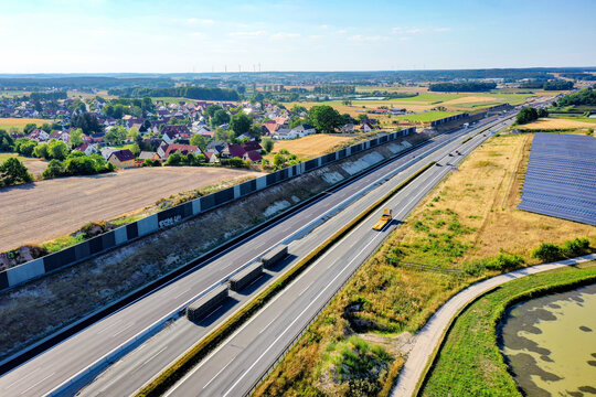Nurnberg, Germany - 18 May 2024: Aerial view of the A73 highway with noise protection walls, trucks, and solar panels near a village in Bayern.