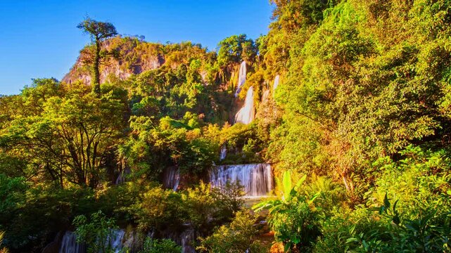 Time lapse scenery of Thi Lor Su Waterfall surrounded by pristine rainforest, dramatic mountain landscapes, and beautiful blue skies during the rainy season in Umphang Wildlife Sanctuary.