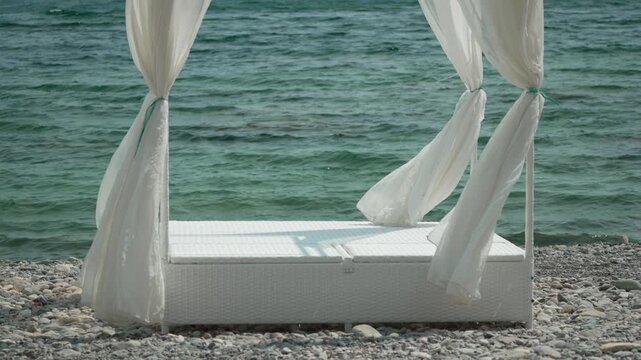Beach cabana ocean, white daybed with curtains on pebble shore, tranquil summer vacation scene.