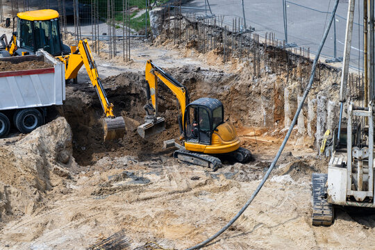 an active construction site where yellow excavators are digging a deep foundation pit and loading dirt into a dump truck.