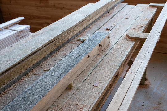 ong wooden planks and an weathered timber beam resting on a sawdust-covered workbench inside a carpenter's workshop.