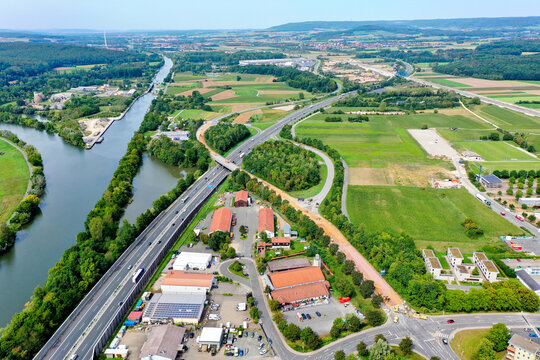 Forchheim, Germany - 02 May 2026: Aerial view of the A73 motorway crossing through a landscape with the Main-Donau-Kanal, industrial buildings, and green agricultural fields.