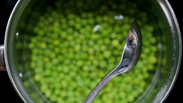 Fresh green peas being boiled in hot water inside a silver kitchen pot.