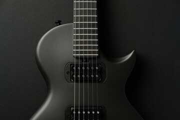 Fototapeta premium Close-up detail of a sleek matte black electric guitar body on a solid black surface.