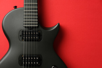 Fototapeta premium High contrast music flat lay. Sleek matte black electric guitar body on a vibrant red background with ample copy space.