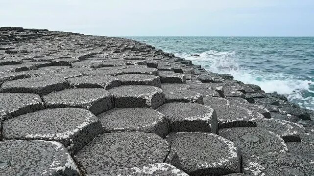 Unique hexagonal rock formations meet the sea in a dramatic coastal landscape.