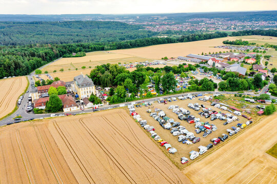 Eggolsheim, Germany - 09 May 2026: Aerial view of Schloss Jagersburg surrounded by lush trees, parking lots filled with vehicles, and golden fields.