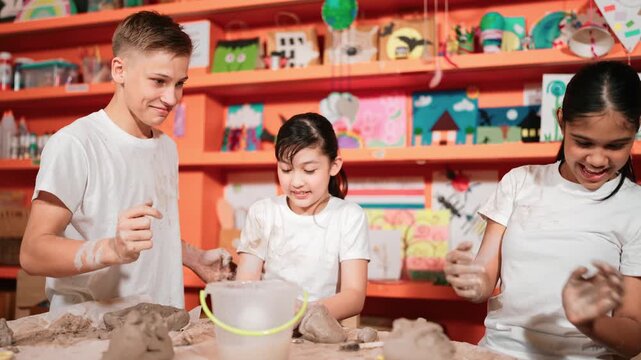 Multicultural happy student playing by throw clay while modeling cup in pottery class. Caucasian high school girl pointing at boy while smiling smart boy laughing at art lesson. Education. Edification