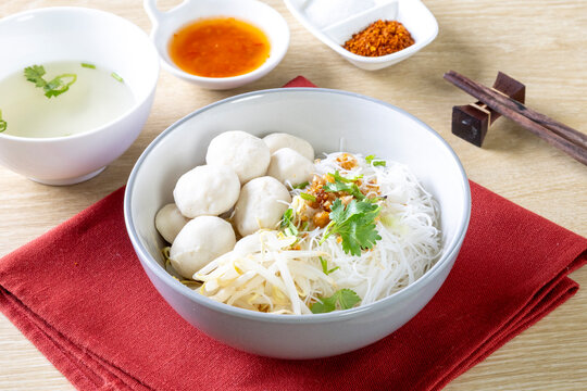 Dry noodles with pork meatballs in a gray bowl on a wooden table.