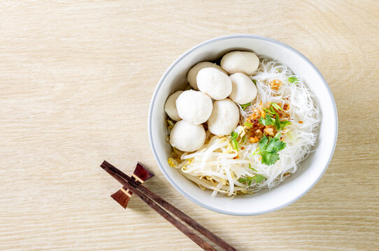 Dry noodles with pork meatballs in a gray bowl on a wooden table.