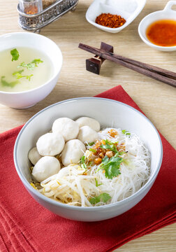 Dry noodles with pork meatballs in a gray bowl on a wooden table.
