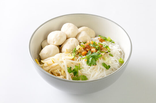 Dry noodles with pork meatballs in a gray bowl on a white background.