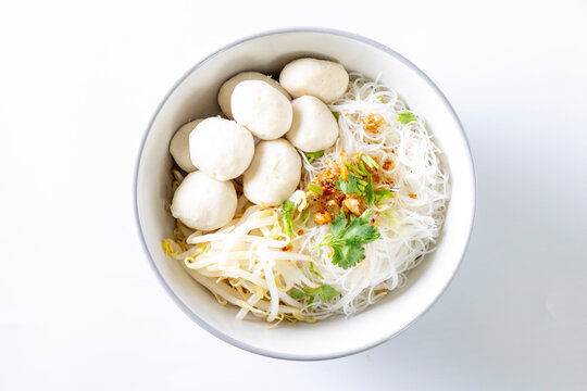 Dry noodles with pork meatballs in a gray bowl on a white background.