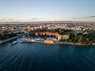 Fototapeta premium Croatia - 05 17 2025: Angled drone photo of Zadar coastline at sunset, showing Adriatic Sea on the left, city buildings on the right, Vladmir Nazor’s Grammar School centered, Molo Terraferma Marina