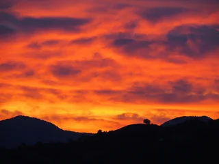 Fototapete Rot Dramatic red and orange sunset sky over mountain silhouettes.  © Patrizia