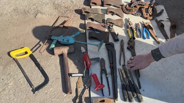 Assorted tools laid on asphalt sunlit display of vintage wrenches chisels hand drill hacksaw axes horseshoes arranged for sale