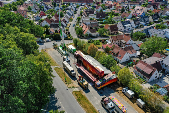 Forchheim, Germany - 19 July 2025: Aerial view of the Annafest fairground setup with a large crane and colorful trucks next to a residential area and lush green forest.