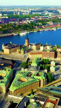 Vertical video. Stockholm, Sweden. Riddarholmen Church, its cast-iron spire rising above the island's historic palaces, aerial panoramic view over Lake Malaren and Gamla Stan under clear summer light