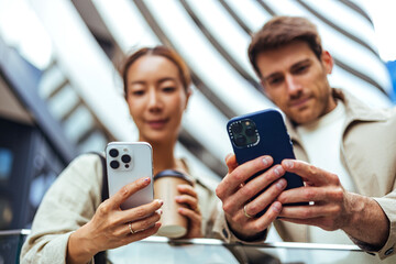 Fototapeta premium Young Couple Using Smartphones Together in Urban Setting With Coffee and Modern Architecture