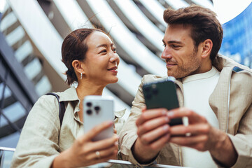 Young Couple Sharing Phones and Smiles in Urban Setting, Modern Connection and Communication © Dragana Gordic