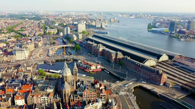 Amsterdam, Netherlands. Amsterdam Centraal station, its Gothic-Renaissance Revival facade and twin turrets rising beside the sweeping cast-iron platform roof, Drone footage over the IJ waterfront. Dr