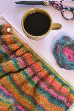 hand knitting making a sweater from self striping alpaca wool on table with cup of coffee and scissors 