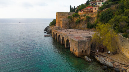 Naklejka premium Alanya, Turkey. Low altitude drone flight past historic Alanya Tersanesi shipyard showing stone arches and medieval architecture from sea view.. Aerial View