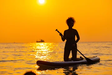 Fototapeten Extremsportarten Woman Paddleboarding Silhouette at Golden Sunset Sea  © Washburn