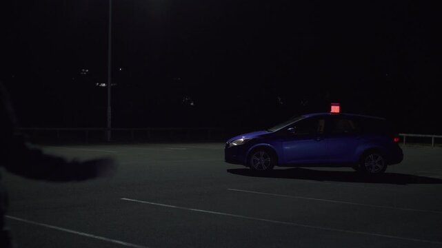 Man surrendering to police beside patrol car with flashing emergency lights at night, placing hands behind head 
