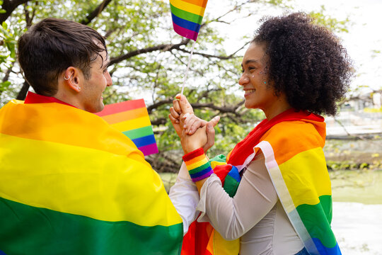 Young LGBTQ Couple Making Heart Shape with Rainbow Flags in Park