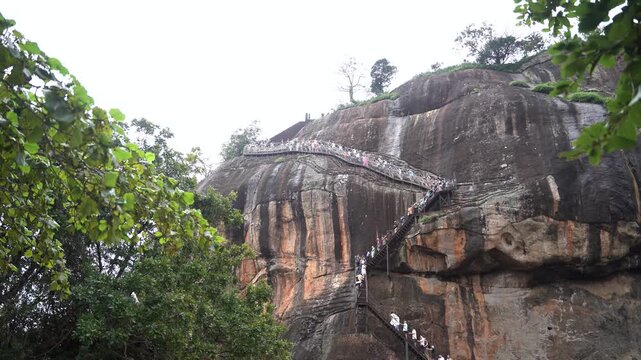 Sri Lanka - 21 May 2026: View of tourists climbing the steep metal staircase on the side of the ancient Sigiriya rock fortress surrounded by lush green trees and vegetation.