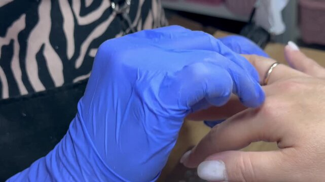 Video of a nail technician filing nails. Manicurist shapes nail using salon nail file during cosmetic procedure in beauty salon. Woman gets a french manicure at a beauty salon, manicurist files her cu