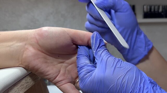 Video of a nail technician filing nails. Manicurist shapes nail using salon nail file during cosmetic procedure in beauty salon. Woman gets a french manicure at a beauty salon, manicurist files her cu