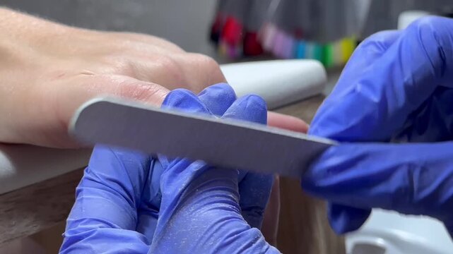 Video of a nail technician filing nails. Manicurist shapes nail using salon nail file during cosmetic procedure in beauty salon. Woman gets a french manicure at a beauty salon, manicurist files her cu