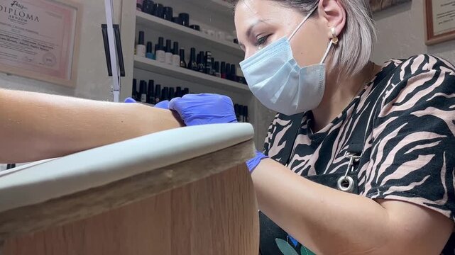 Video of a nail technician filing nails. Manicurist shapes nail using salon nail file during cosmetic procedure in beauty salon. Woman gets a french manicure at a beauty salon, manicurist files her cu