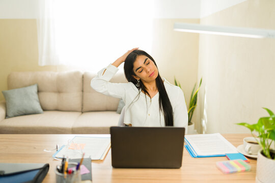 Stressed woman stretching neck muscles at desk working from home, relieving pain during remote business workday