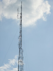 Obraz premium A tall metal telecommunications antenna mast stands against a blue sky with soft white clouds.