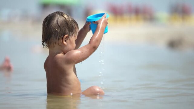 Kid collects shells and pebbles in the sea on a sandy bottom under the summer sun on a vacation