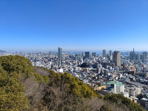 Stunning aerial daytime view of Kobe cityscape with skyscrapers, Kobe Port Tower, and Osaka Bay under a clear blue sky, Japan