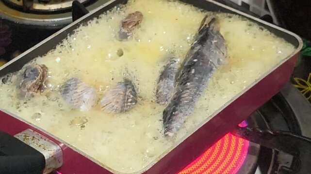 Close-up shot of fish and mussels cooking in a pot of boiling white wine on a red stovetop with a dark background.