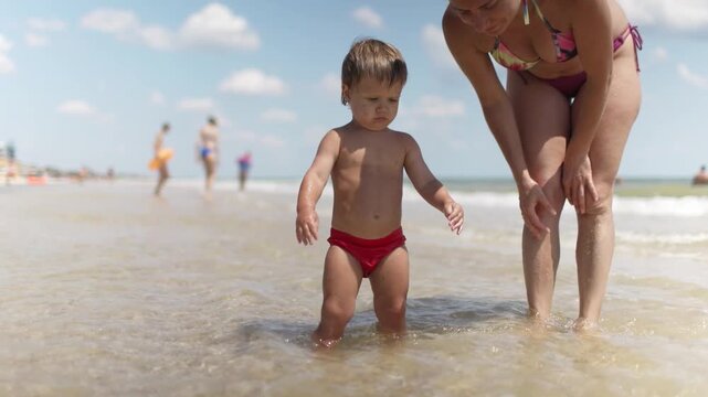 The kid collects shells and pebbles in the sea on a sandy bottom with his mother under the summer sun on vacation