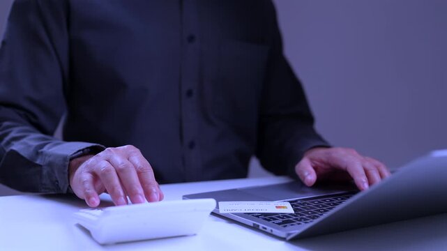 Close view focused male clerk wearing dark shirt types laptop keys, does budget sums operating calculator, checking work financial business data inside modern office, showing video player interface.