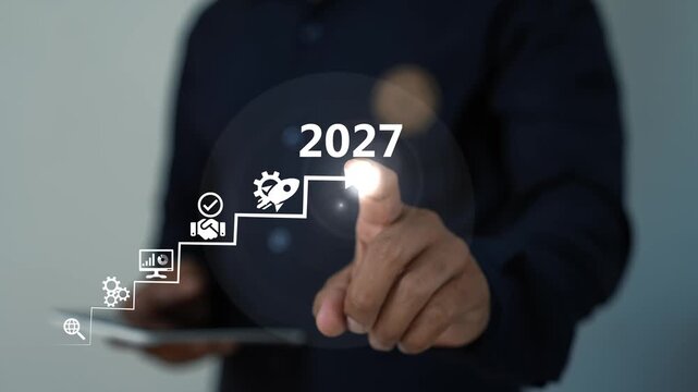 Businessman pressing 2027 with digital icons on the virtual screen, Hand pointing at glowing 2027 step graphic with icons