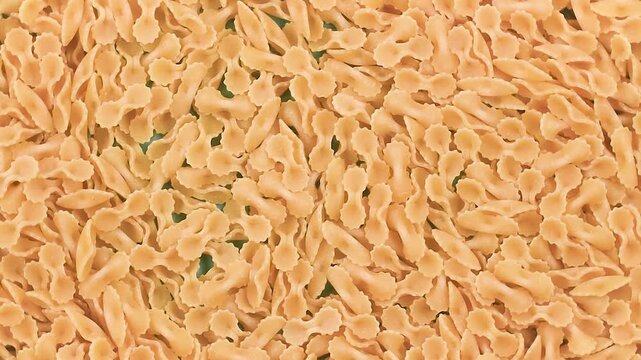 Rotating video of uncooked Farfalline pasta with tiny bow tie shapes and textured edges, highlighting golden wheat color and detailed Italian pasta patterns in smooth close-up motion.