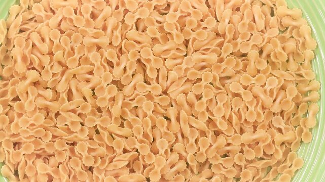Rotating video of uncooked Farfalline pasta with delicate bow tie shapes and textured edges, showcasing golden wheat color and detailed Italian pasta patterns in close-up motion.