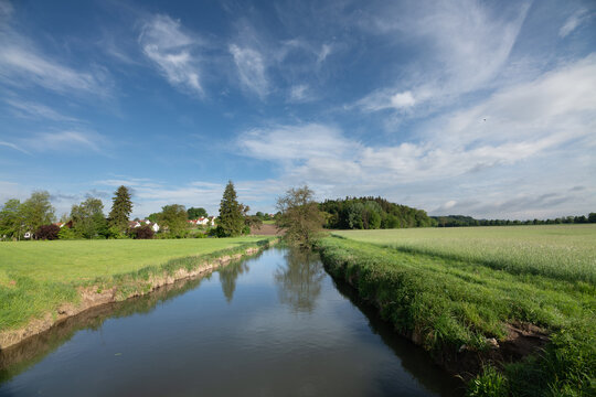 A narrow river winds its way through a lovely landscape. The blue sky is reflected in the water.