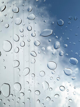Large rain droplets on a window with dramatic cloudy sky and power lines visible in the background. Atmospheric weather and transportation concept.