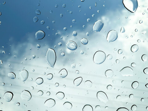 Large rain droplets on a window with dramatic cloudy sky and power lines visible in the background. Atmospheric weather and transportation concept.